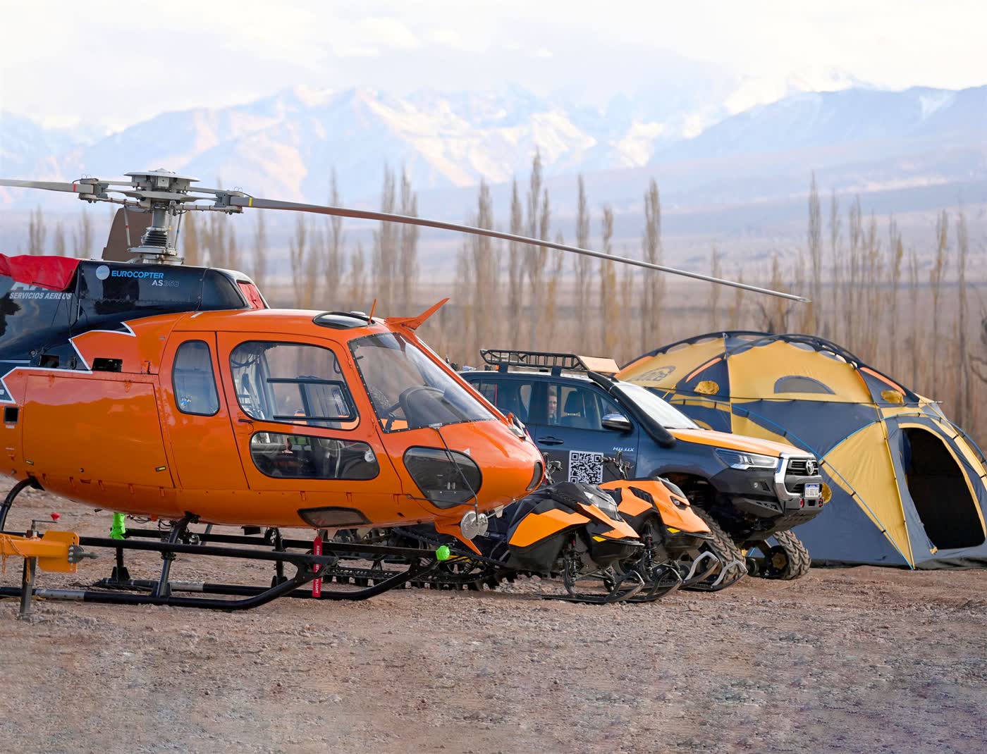 Helicopter, snowmobiles and pickup truck from the GHM fleet in front of the Andes